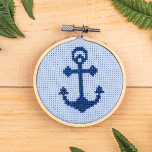 Product shot of a finished cross stitch hoop. It is a dark blue anchor on a blue background.