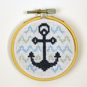 A finished cross stitch hoop of an anchor with waves in the background