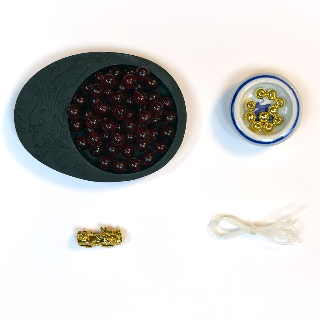 Red and gold beads in dishes with a large gold dragon bead and elastic stretchy cord